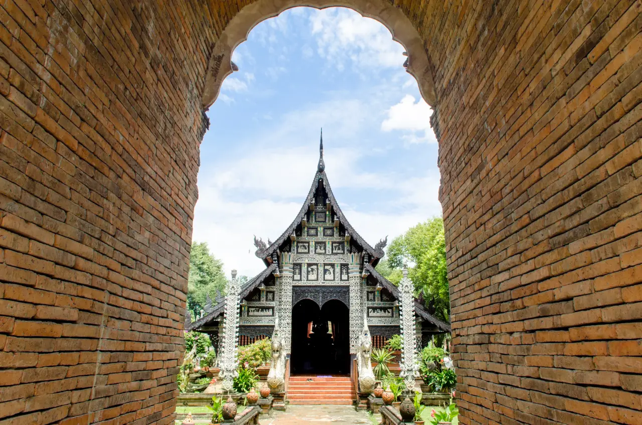 Sunlit Lanna temple hall framed by the brick gateway at Wat Lok Moli in Chiang Mai