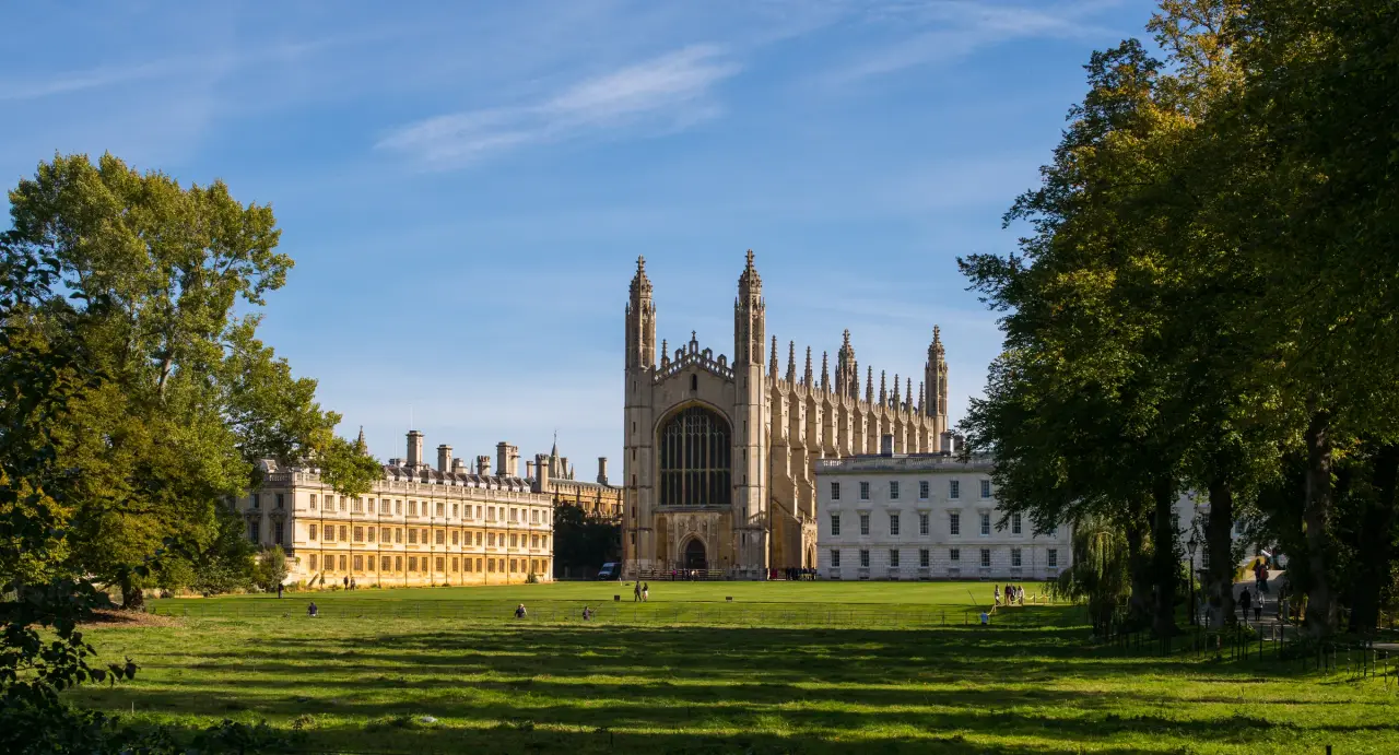 King’s College Chapel beyond sunlit green lawns and trees beside the River Cam in Cambridge.