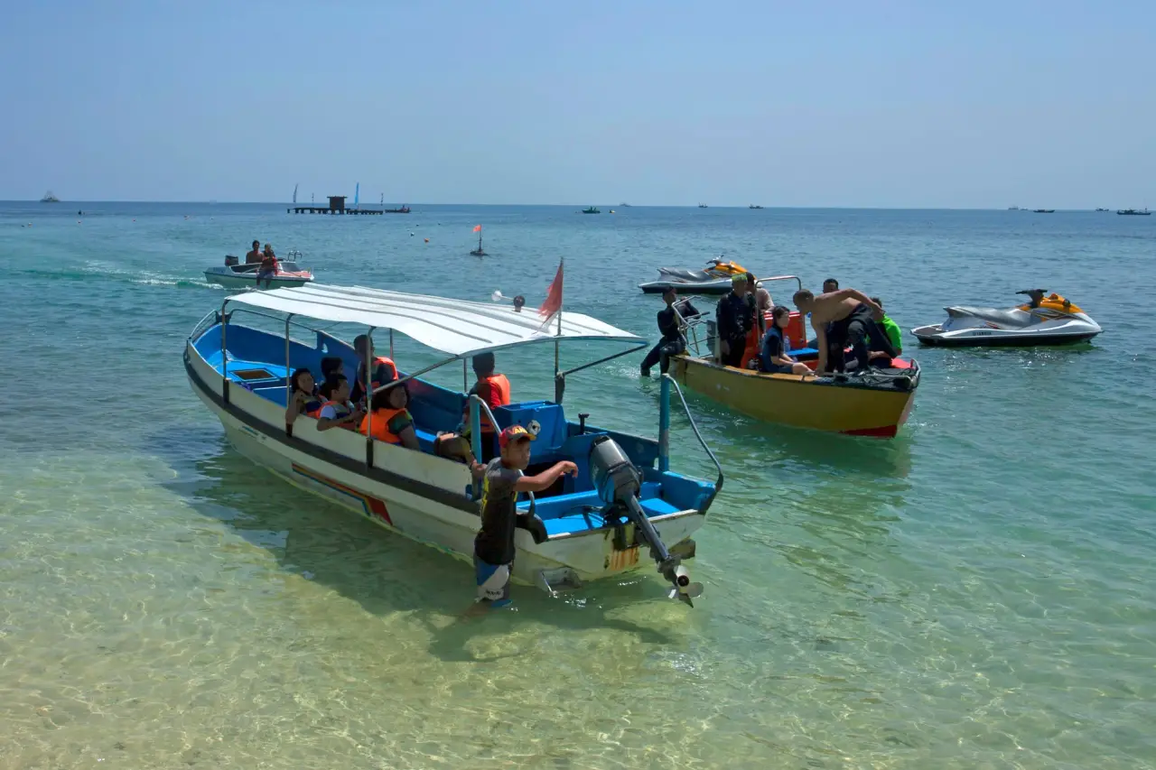 Passengers sit aboard a covered blue-and-white boat in clear shallow water.