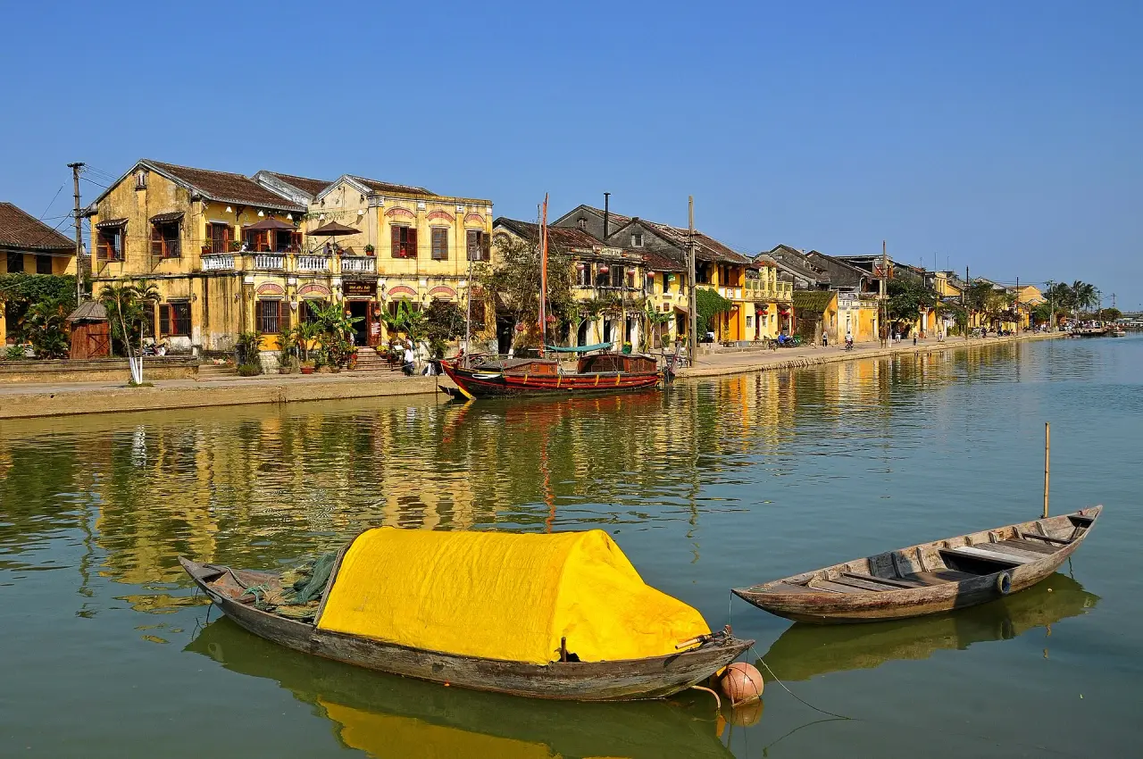 Yellow riverside buildings and small boats reflected in the water at Hoi An Ancient Town in clear daylight