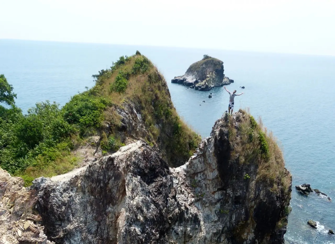 A rugged coastal headland and offshore rocks on Ko Lanta, Thailand, with a distant visitor