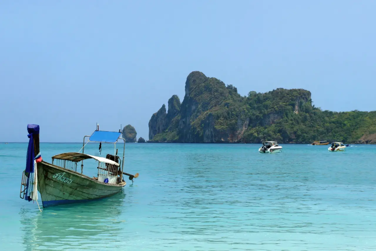 A traditional longtail boat floats in turquoise water beside a limestone island.